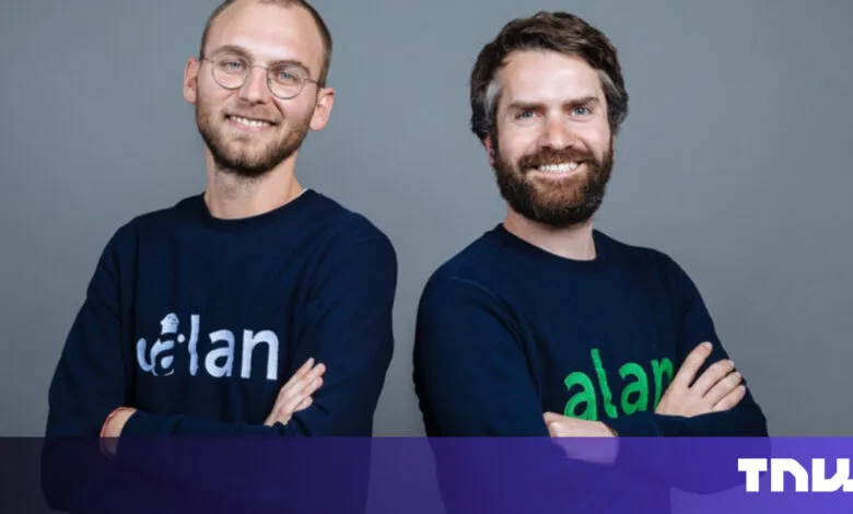 Two men smiling, wearing branded sweaters against a gray background.