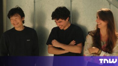 Three smiling young adults stand side-by-side against a textured wall.
