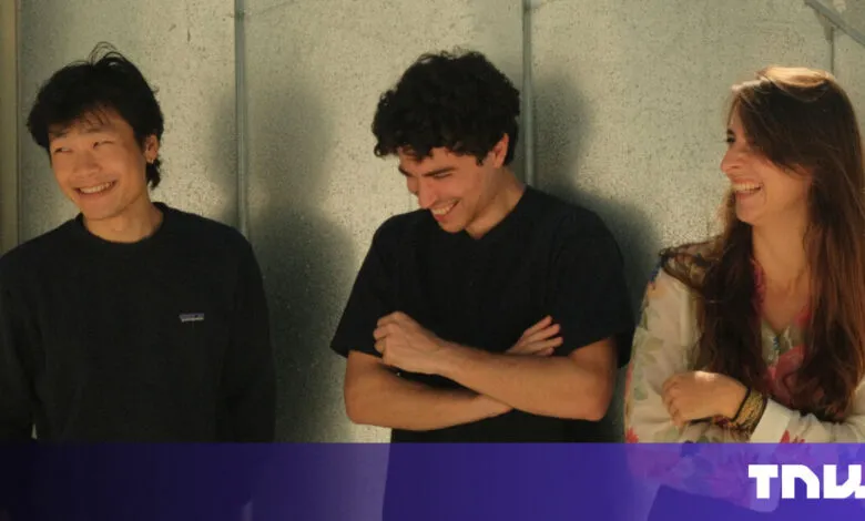Three smiling young adults stand side-by-side against a textured wall.