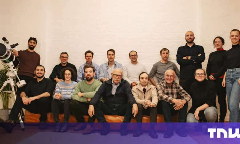 Group of diverse people pose together in front of a white brick wall.