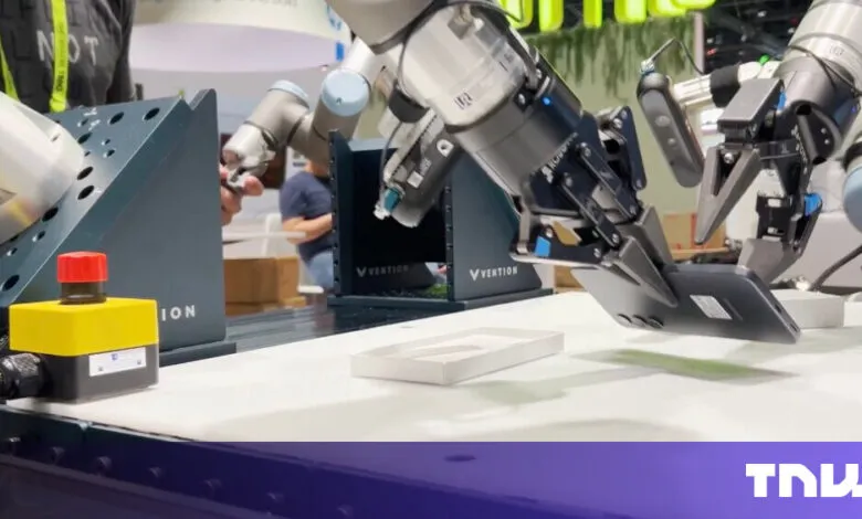 Robotic arms assembling a smartphone on a white conveyor belt.