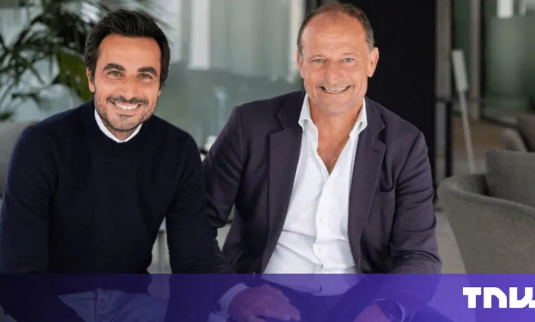 Two smiling men pose indoors in business attire.