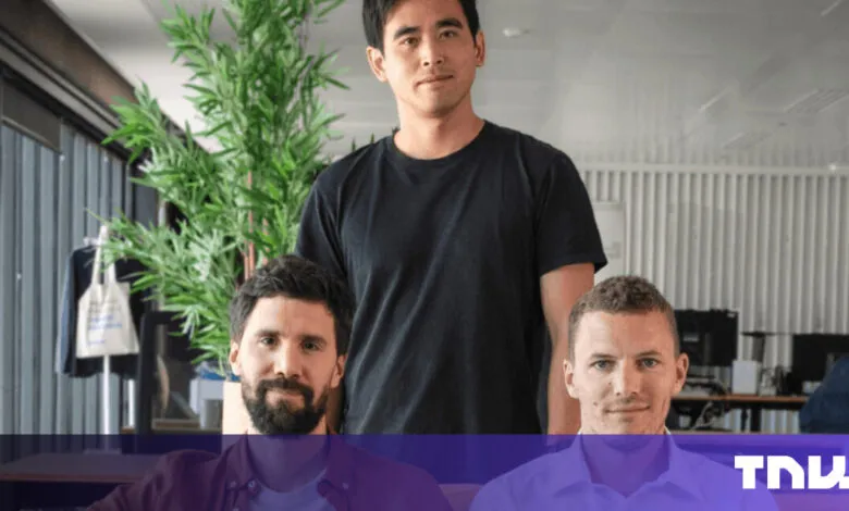 Three men pose indoors, one standing behind two seated figures.