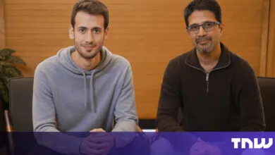 Two men sit side-by-side in chairs, looking at the camera.