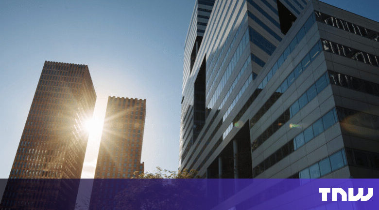 Modern office buildings rise against a clear blue sky, sunlight reflecting off windows.
