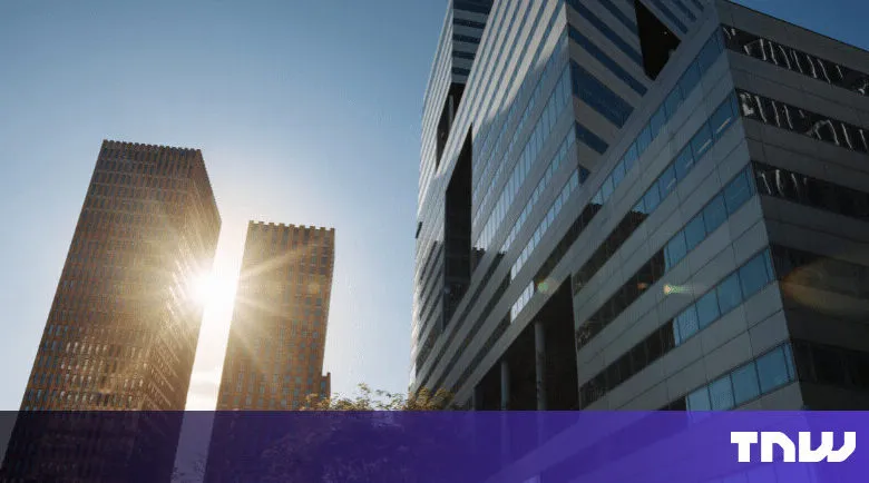 Modern office buildings rise against a clear blue sky, sunlight reflecting off windows.