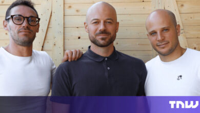 Three men stand side-by-side in front of a wooden wall.