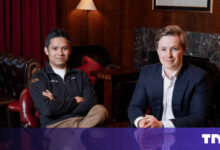 Two men pose indoors in a sophisticated setting.