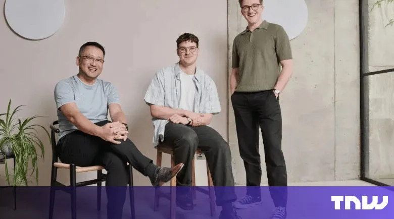 Three men pose indoors, seated and standing, in casual attire.