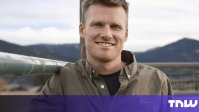 Smiling man in olive shirt leaning on metal railing outdoors.