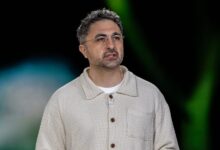 Man with glasses and textured shirt speaks on stage.