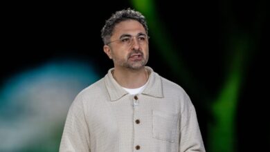 Man with glasses and textured shirt speaks on stage.