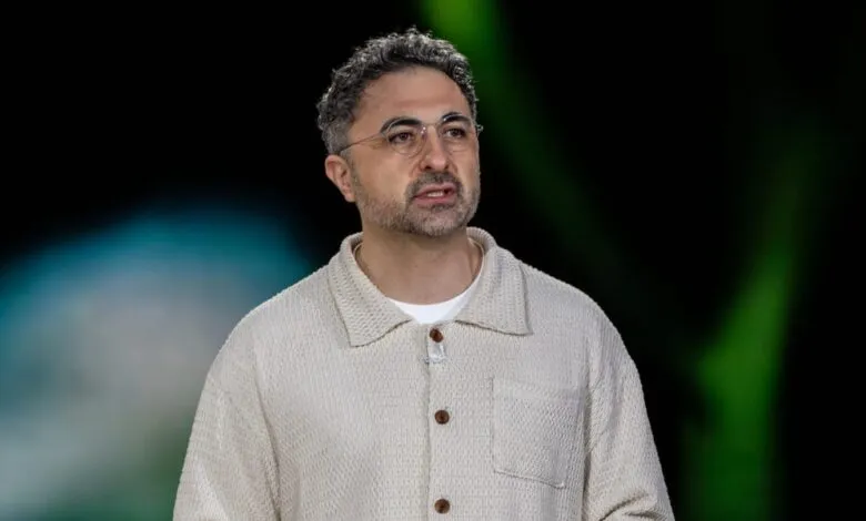 Man with glasses and textured shirt speaks on stage.