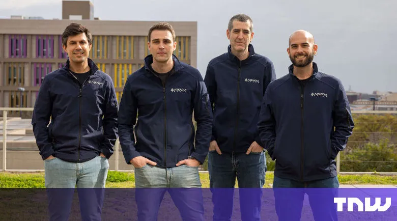 Four men in matching jackets stand outdoors, smiling at the camera.