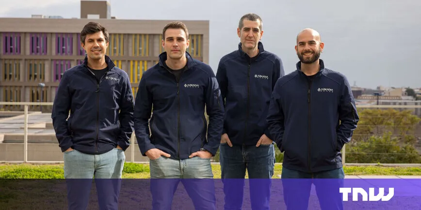 Four men in matching jackets stand outdoors, smiling at the camera.