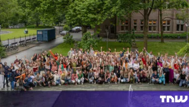 Large group of people waving in front of a building and park.