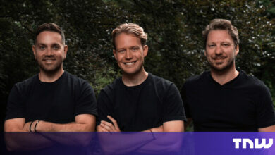 Three men stand smiling with arms crossed against a leafy backdrop.