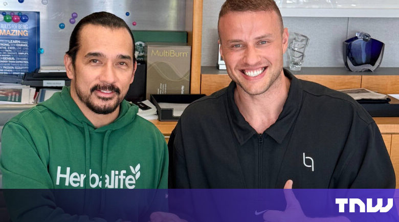Two men smiling, one wearing Herbalife hoodie, the other a black jacket.