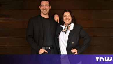 Two smiling professionals pose in front of a wood-paneled wall.