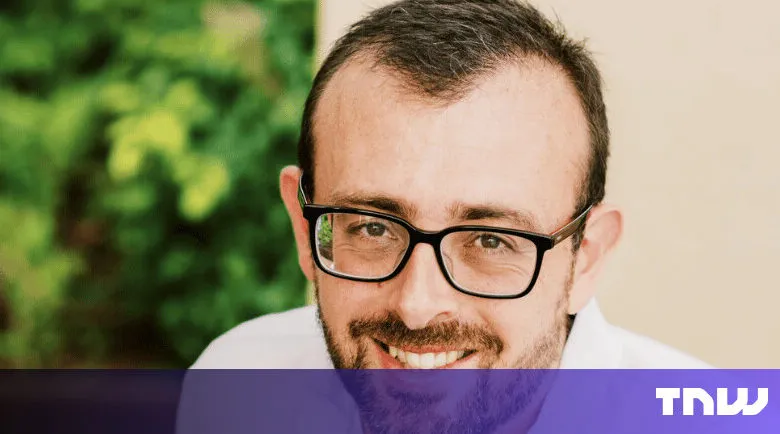 Close-up of smiling man with glasses against a blurred green background.