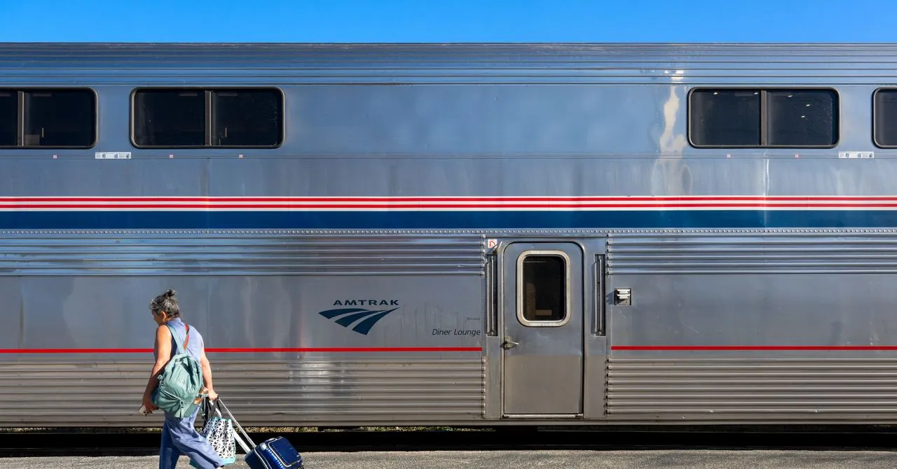 Woman walks past Amtrak train with luggage and backpack.