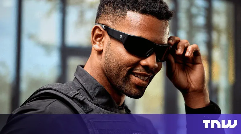 Man in tactical gear adjusts smart glasses, smiling slightly.