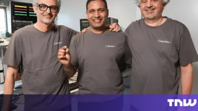 Three men in matching shirts pose in a tech lab setting.