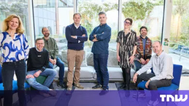 Group of eight people posing indoors with large windows and natural light.