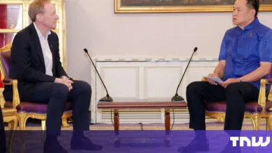 Two men sit facing each other in ornate chairs, microphones between them.