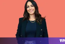 Smiling woman in blazer against coral backdrop.