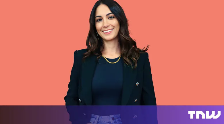 Smiling woman in blazer against coral backdrop.