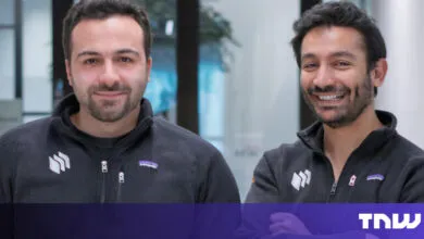 Two smiling men stand side-by-side in matching gray zip-up sweaters.