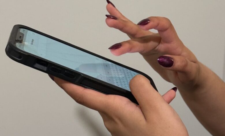 Hands with long, dark red nails typing on a smartphone.