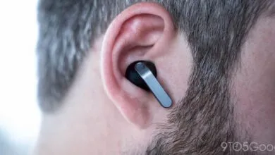 Close-up of black wireless earbud with silver accent in a person's ear.