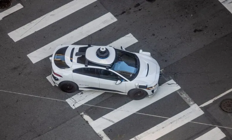 Aerial view of a white Waymo self-driving car crossing a street at a crosswalk.