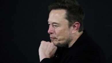 Elon Musk in profile with hand on chin against a dark background.