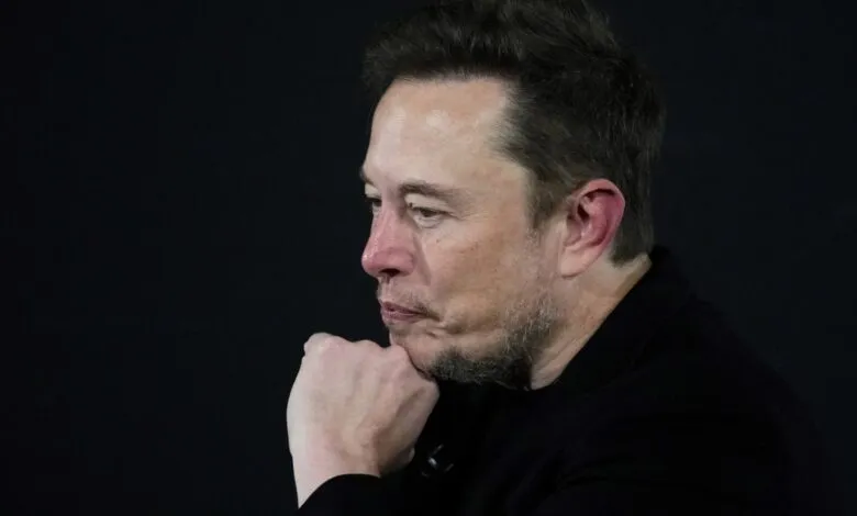 Elon Musk in profile with hand on chin against a dark background.