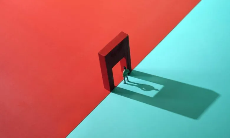 Miniature figure stands in doorway between red and blue backgrounds.