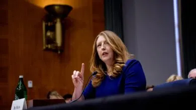 Woman in blue dress speaks at a hearing, raising her index finger.