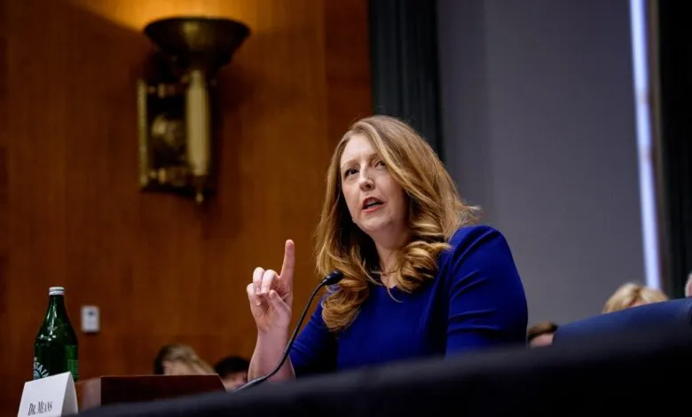 Woman in blue dress speaks at a hearing, raising her index finger.