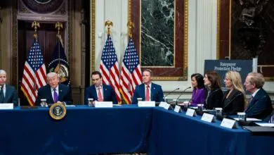 Donald Trump at a table with others, American flags behind him.
