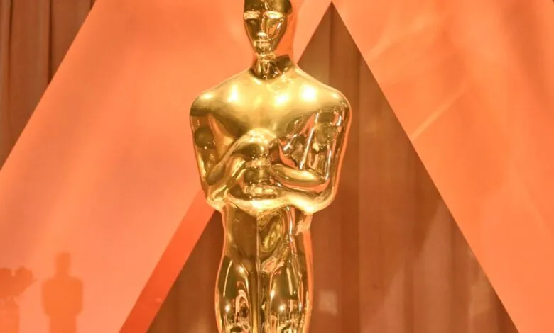 Close-up of a golden Oscar statue against an orange backdrop.