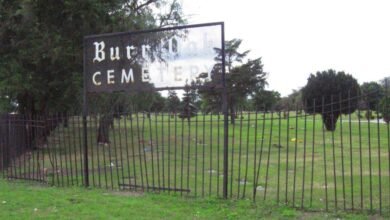Entrance to Burr Oak Cemetery with a metal sign and wrought iron fence.