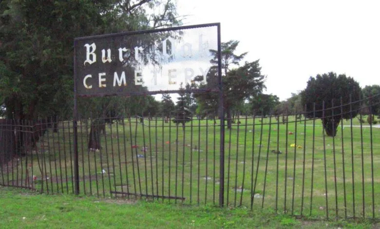 Entrance to Burr Oak Cemetery with a metal sign and wrought iron fence.
