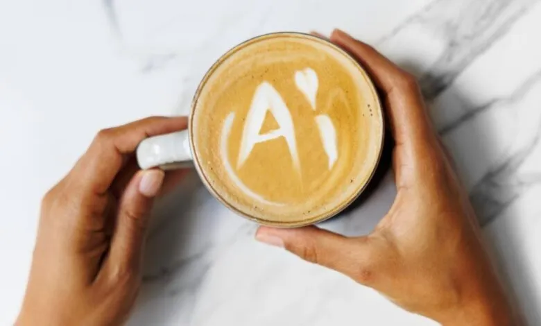 Hands hold coffee cup with 'AI' latte art on marble background.
