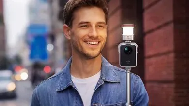 Smiling man holds camera with light on city street.