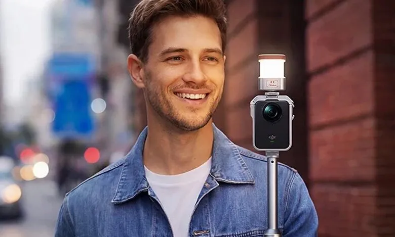 Smiling man holds camera with light on city street.