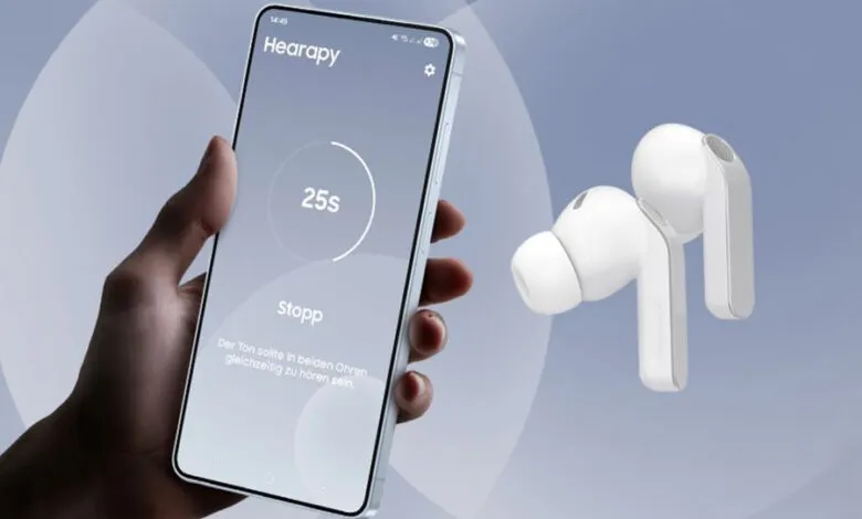 Hand holding phone with Hearapy app next to white wireless earbuds.