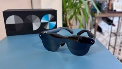 Smart glasses on a blue surface with a box and plant in the background.
