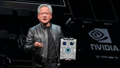 Jensen Huang holds a circuit board in front of an Nvidia backdrop.